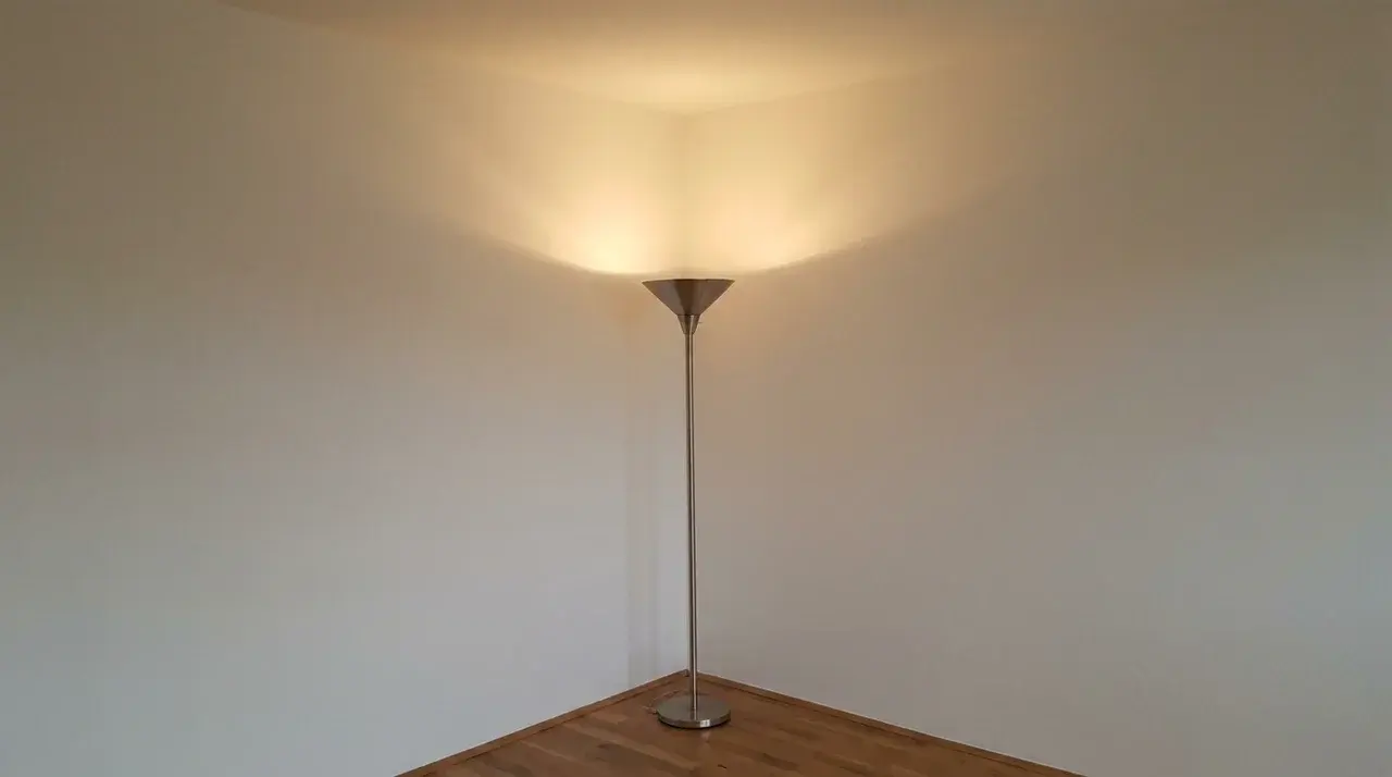Floor lamp in bare room corner casting warm light upward and outward along both walls