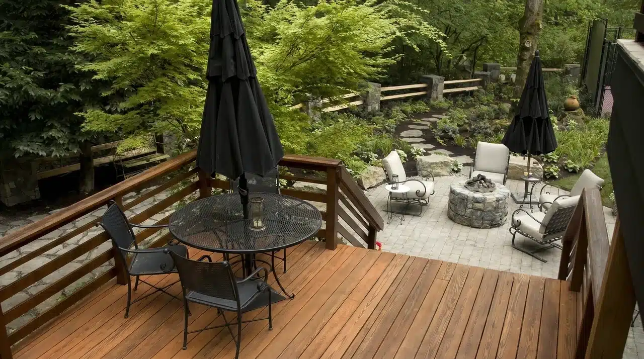 Rich chestnut wood deck with dark metal furniture and stone patio surrounded by Japanese maple trees