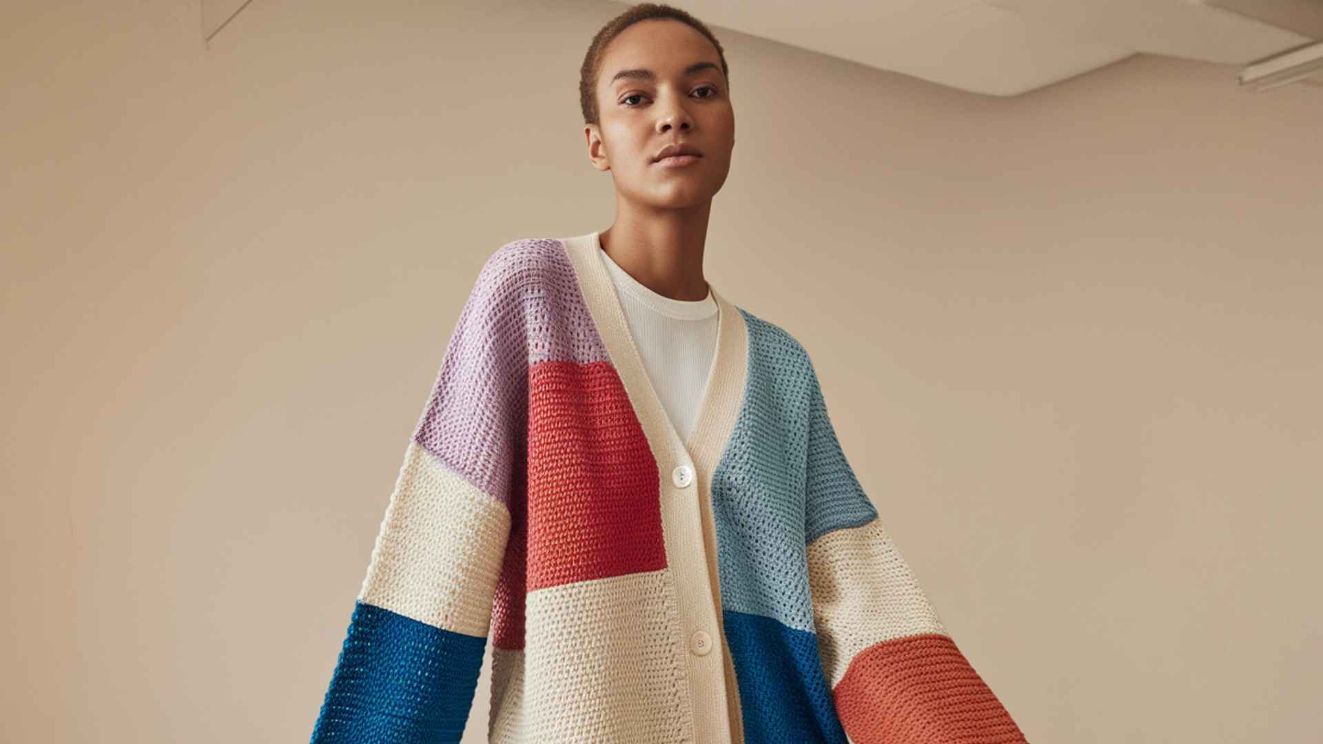 Waist-up model wearing a color block crochet cardigan with contrasting panels.