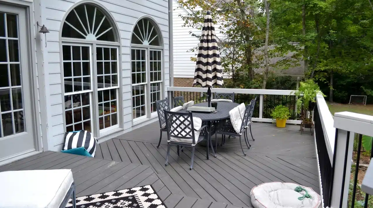 Charcoal gray deck with white railing and black metal furniture on a white traditional home exterior