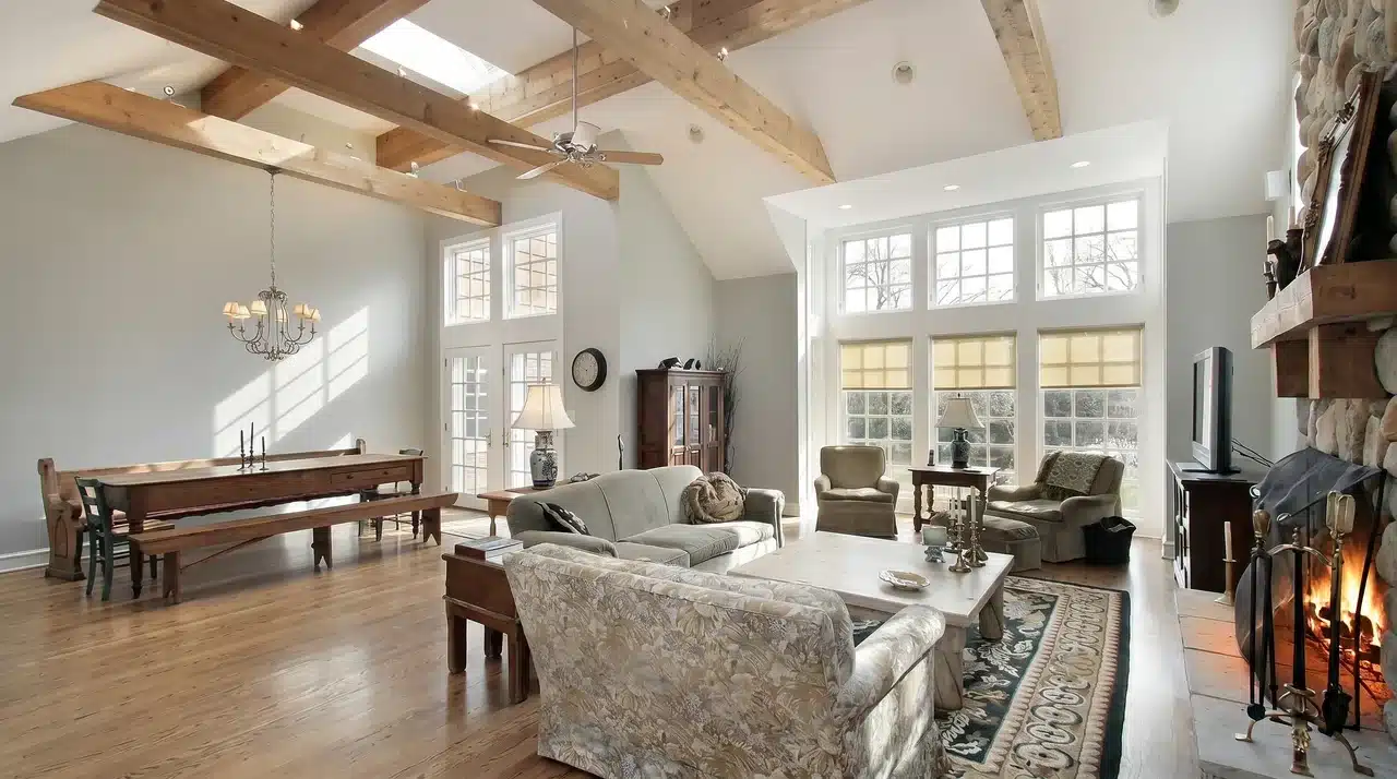 Sun washed French country living room with exposed wood ceiling beams, stone fireplace, farmhouse dining table, and wide plank floors